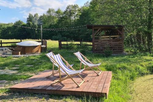 two chairs sitting on a wooden deck in the grass at Domek z Sauną i balią jakuzii w głuszy in Borzynowo