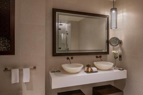 a bathroom with two sinks and a mirror at Alwadi Hotel Doha - MGallery Collection in Doha