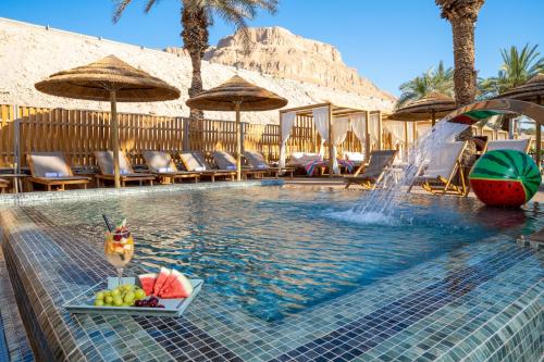 a swimming pool with a bowl of fruit and a fountain at Oasis Spa Club Dead Sea Hotel - 18 Plus in Ein Bokek