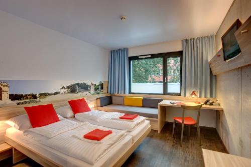 a bedroom with two beds and a desk and a television at MEININGER Hotel Wien Downtown Franz in Vienna