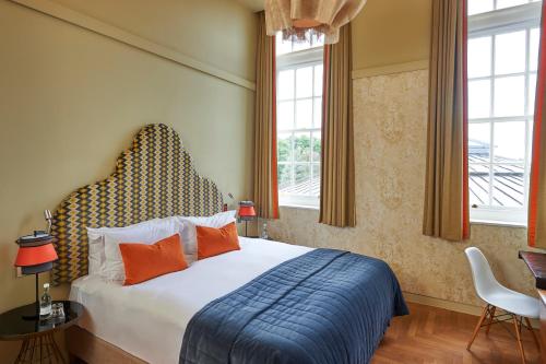 a bedroom with a bed with orange pillows and windows at Hotel du Vin Exeter in Exeter