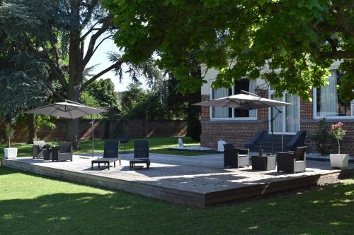 a patio with chairs and umbrellas in a yard at Logis Manoir de Fourcy in Corbehem