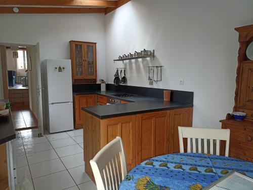 a kitchen with a table and a white refrigerator at Maison Marin, Charming Village Cottage with Pool in Saint-Thomas-de-Cônac