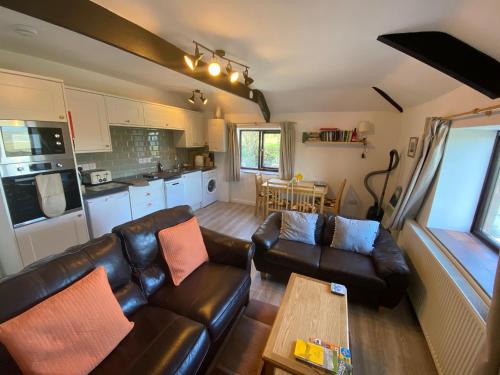 een woonkamer met een leren bank en een tafel bij Polrunny Farm Elderberry Cottage with sea view in Boscastle