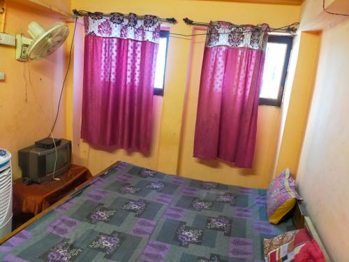 1 dormitorio con cortinas rosas, 1 cama y TV en Maa Vaishno Guest House, en Varanasi