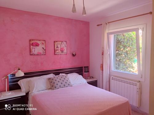 um quarto com uma parede cor-de-rosa, uma cama e uma janela. em Galdana Sun And Beach em Cala Galdana