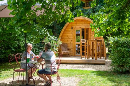 a man and woman sitting at a table in front of a wooden cabin at Cabane en bois avec bain nordique in Asnières-sur-Vègre