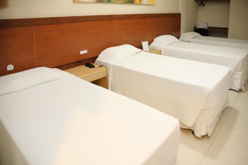 a row of beds in a room with white sheets at Rede Andrade Vivaldi in Foz do Iguaçu