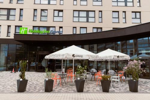 two tables and chairs with umbrellas in front of a building at Holiday Inn Express Warsaw - Mokotow by IHG in Warsaw