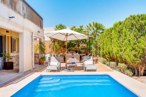 a pool with chairs and an umbrella next to a house at Villa Cala Estancia Mercedes by PriorityVillas in Palma de Mallorca
