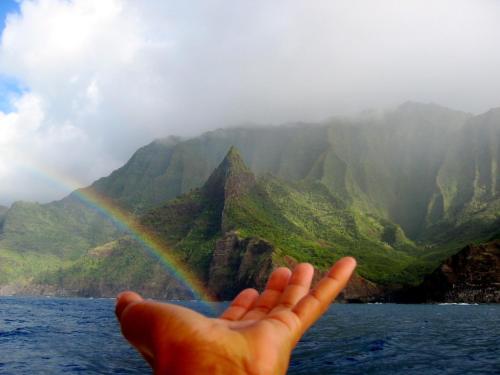a hand with a rainbow in front of a mountain at West Kauai Lodging in Waimea