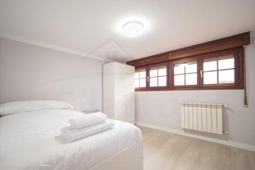 a white bedroom with a bed with towels on it at El Pico, Apartamento in Ribadesella