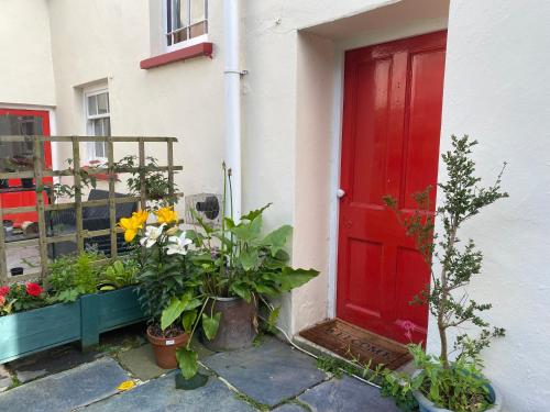 a red door on a house with flowers and plants at Coastal cottage ‘The Old Bank’ in Hartland