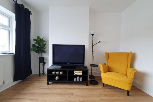 a living room with a tv and a yellow chair at One Bed Apartment With Sofa Bed in Llandudno