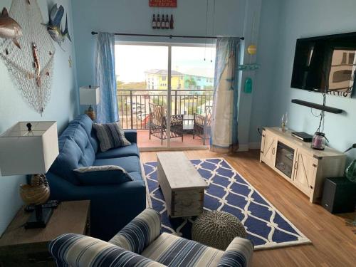 a living room with a blue couch and a tv at Gulf Coast Gold Private Condo - 2bed, 2bath, Sleep 6, Across Street from Beach, Balcony Views Of Sunsets, Beach & Gulf, Pool, Gym in St Pete Beach