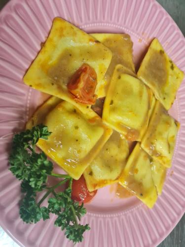 a pink plate of food with ravioli and a tomato at Hotel ristorante Bucaneve in Val Masino