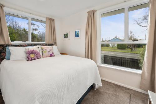 a bedroom with a bed and large windows at Plum Tree Cottage - Turangi Holiday Home in Turangi