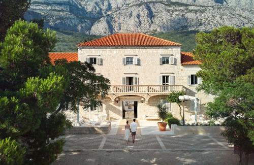 dos personas caminando frente a un gran edificio en Heritage Hotel Kaštelet, en Tučepi