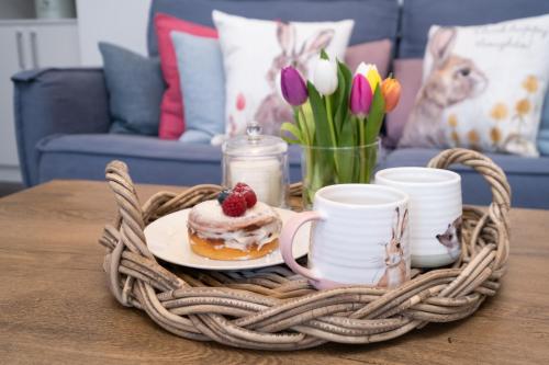 einen Korbkorb mit Gebäck auf einem Tisch mit Tassen und Blumen in der Unterkunft The Garden Cottage of Warren Lodge boutique cottages in Dromod