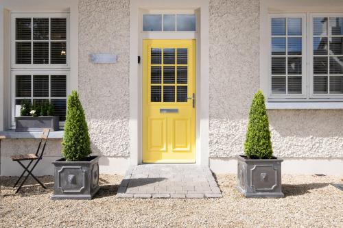 a yellow door on a white house with two plants at The Pine Tree Cottage of Warren Lodge Boutique Cottages in Dromod