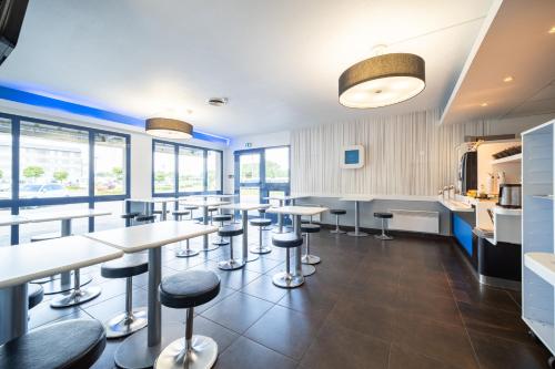 a bar with tables and stools in a room with windows at B&B HOTEL Calais Terminal Cité Europe 2 étoiles in Coquelles