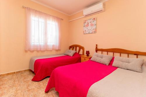 a bedroom with two beds with red sheets and a window at MI PERLA in Torrevieja
