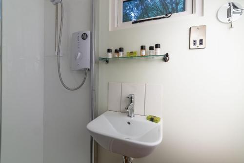 La salle de bains est pourvue d'un lavabo blanc et d'une douche. dans l'établissement Woodland Retreat Shepherd's Hut, à Brundish