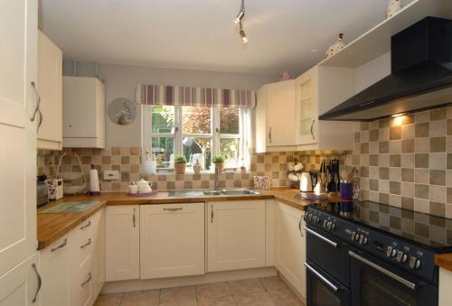 a kitchen with white cabinets and a sink and a window at Little Shrublands in Blockley