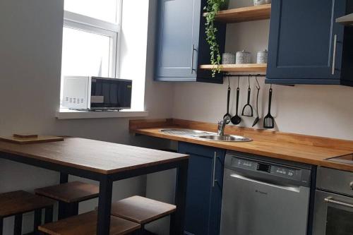 a kitchen with blue cabinets and a sink and a table at Sea Reach Apartment, 2 minutes from beach and town in Newquay