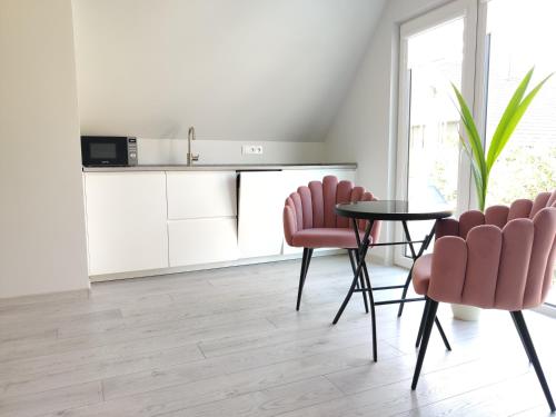 kuchnia z białymi szafkami, różowymi krzesłami i stołem w obiekcie Neringos 22 w Połądze