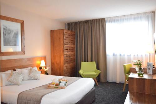 a hotel room with a bed and a green chair at Kyriad Prestige - Bordeaux Aeroport in Mérignac