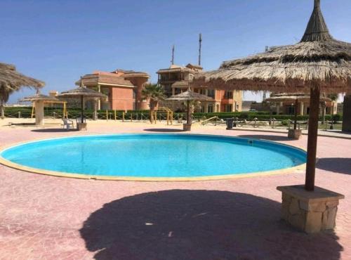 a large swimming pool with a straw umbrella at Blumar North Coast in El Alamein