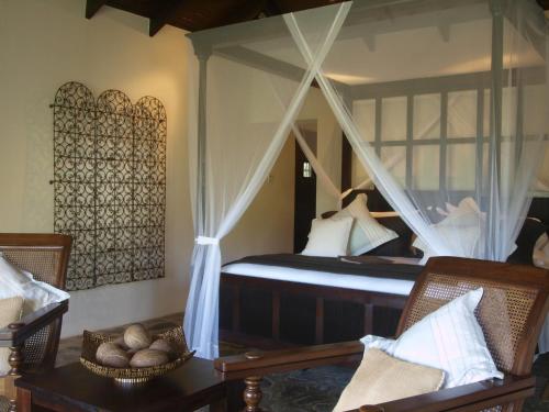 a bedroom with a canopy bed and two chairs at Firefly Estate Bequia in Crescent Beach