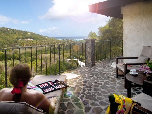 a woman sitting on a chair on a balcony looking at the ocean at Firefly Estate Bequia in Crescent Beach
