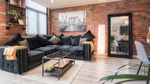 ein Wohnzimmer mit einem schwarzen Sofa und einer Ziegelwand in der Unterkunft Stunning 2 bed with outside balcony, super king beds and 75’’ TV! in Bradford