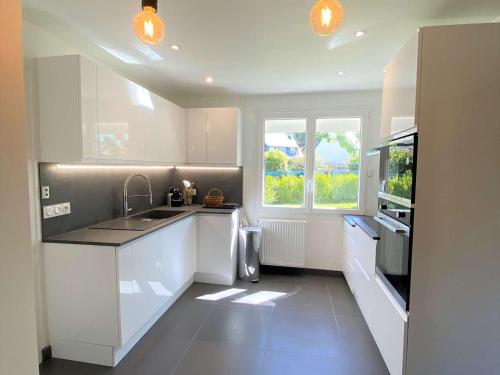 une cuisine avec des armoires blanches, un évier et une fenêtre dans l'établissement Grande maison 4* à Beg Meil avec jardin, à 1 km de la plage - FR-1-481-119, à Fouesnant