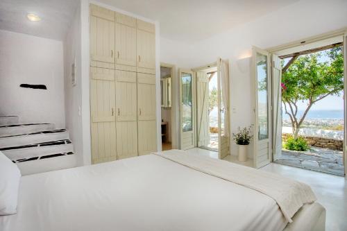 ein weißes Schlafzimmer mit einem großen Bett und großen Fenstern in der Unterkunft Lithos Villas in Karystos