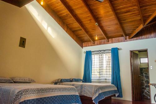 a bedroom with two beds and a window with blue curtains at Vista Lago Arenal in Piedras