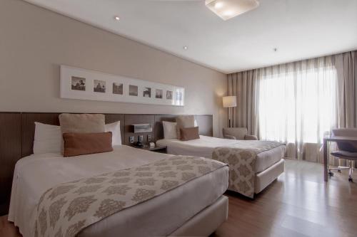a hotel room with two beds and a table at Hotel Deville Prime Porto Alegre in Porto Alegre