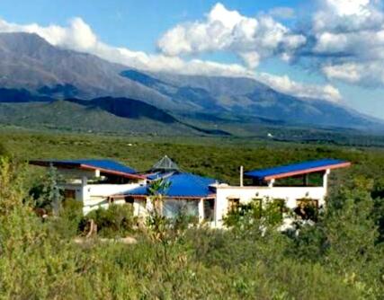Un edificio con tejados azules y montañas al fondo. en Refugio: El Llamado, en Villa Las Rosas