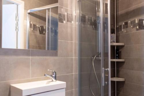 une salle de bain avec une douche avec un lavabo et un miroir dans l'établissement LOC TROTTEUR LE GRAPHITE T2 Grand confort Terrasse, à Lourdes