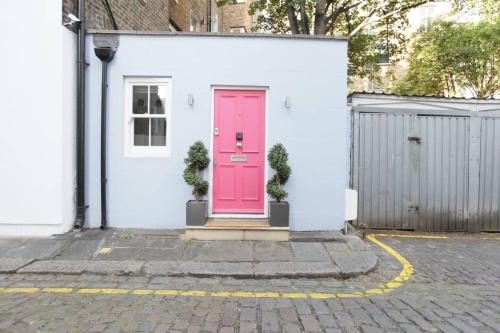 eine rosa Tür auf einem weißen Haus mit zwei Pflanzen in der Unterkunft Newly Refurbished 1 Bedroom in Vibrant Notting Hill in London