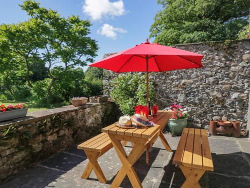 a picnic table with a red umbrella on a patio at Beckside Farm in Millom