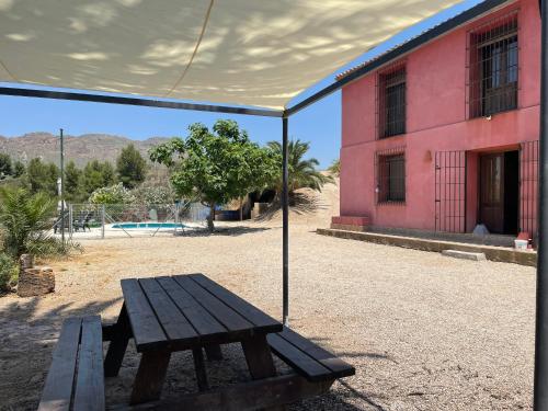 a wooden picnic table under a tent next to a pink building at Casa Ramoncico. Finca el Campillo in Blanca