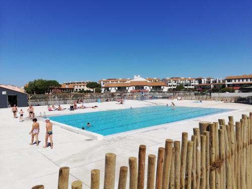 a swimming pool with people standing around it at Style Bord de mer avec une chambre et une terrasse extérieure - PISCINE OUVERTE et CHAUFFÉE - Vue lac - Aire Jeux d' Enfants - Check-in Automatisé - Parking gratuit - au bord du lac - Animations Juillet Août in Le Barcarès