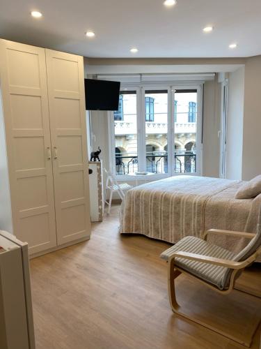 a bedroom with a bed and a chair and a window at Alojamientos Muelle de Gijón in Gijón
