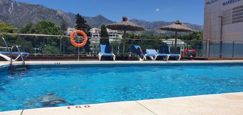 uma piscina com cadeiras e guarda-sóis num edifício em Apartamento con jardín y piscina em Marbella