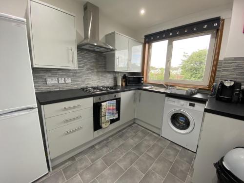 een keuken met witte kasten en een wasmachine bij Pure Apartments Fife - Dunfermline - Pitcorthie in Dunfermline