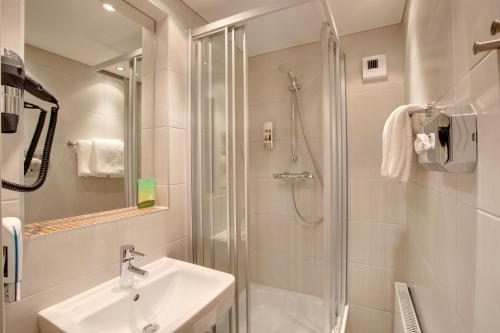 Un baño blanco con lavabo y ducha. en MEININGER Hotel Salzburg City Center, en Salzburgo