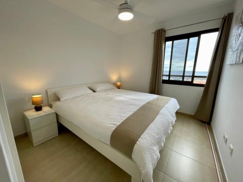 a white bedroom with a bed and a window at Achacay Sunset Apartment in Los Cristianos